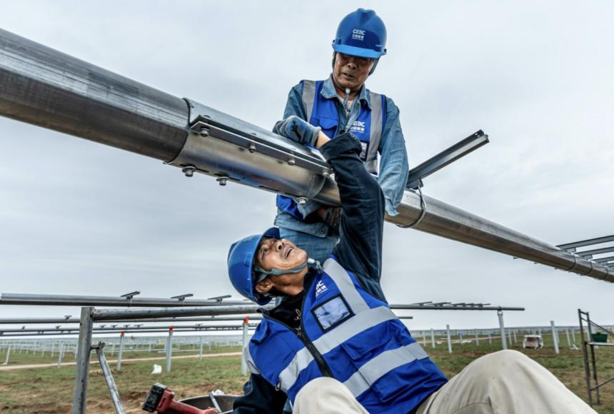 该项目在国内首次大规模应用平单轴H型钢桩作为平单轴基础，相比混凝土预制桩，打桩直径从400毫米降至100毫米，显著减少对草原地貌破坏。平单轴的应用可以实现光伏板追踪太阳自动旋转，大大提升发电效率。近4000名建设者分散在光伏基地各个作业面，他们不舍昼夜、日复一日的辛勤付出，让这片荒凉的土地成功焕发生机，源源不断向外输送清洁能源。图为建设者在紧固平单轴螺栓。