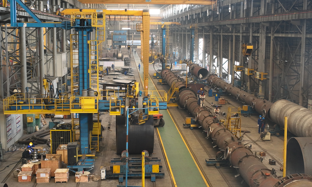 在内蒙古图克工业区的制造现场，上百吨的“庞然大物”被拆解成一块块“积木”：异型锥体被分片压制、组装；数十吨钢板一遍遍“翻身”，10米立车在钢花中精雕细琢……与此同时，1500多公里外的南京车间内，工人们为巨大的“滚筒”喷上白漆，设备内焊花飞溅。这是中建安装旗下中建五洲“现场+工厂”两线制造模式在宝丰项目的再度应用。凭借着全国领先的大型塔器、反应器现场制造水平，项目团队完成了内蒙古宝丰项目反应、换热、分离及储存容器等91台重要设备制造与安装。