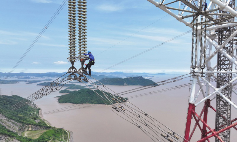 此次检修规模大、技术难度高，洛春5495线、洛晓5496线为跨海输电线路，连接两条线路的两座高370米的输电铁塔分别位于舟山大猫山和宁波凉帽山，两座输电铁塔档距达2756米。检修人员登上位于大猫山的输电铁塔，在高低落差达280米、最低点距海面高度超84米的线路开展走线作业。图为检修人员通过绝缘子串下到跨海输电导线上。