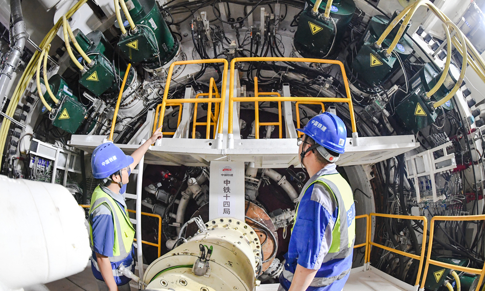 该隧道紧邻海岸线，地下水位高、基岩起伏大、周边建（构）筑物密集，建设条件极其复杂，且盾构隧道有1852米为浅覆土掘进，最浅覆土仅为8.1米，沿线穿越上软下硬、软硬不均、孤石和基岩凸起等复杂地层，中风化花岗岩强度最大达到了134.34兆帕，盾构掘进姿态控制难，易造成“翘头”风险，还需应对高层建筑物锚索、双线隧道小间距等诸多施工难题，对盾构机整机的适应性和刀盘刀具的耐磨性提出了极高要求。图为工程技术人员巡检盾构机运行情况。 