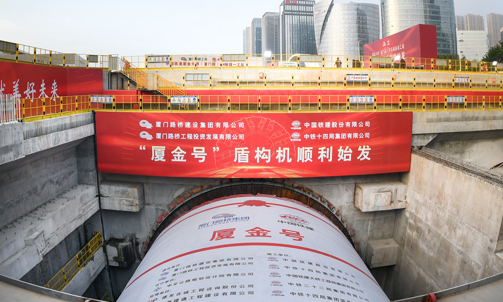 厦金大桥（厦门段）工程起于厦门环岛东路与会展北路交叉口，以隧道形式沿环岛路向北延伸至观音山，往东以桥梁形式跨越本岛东部海域，终点设互通接入厦门翔安国际机场，主线长17.34公里。其中，环岛路隧道长3.29公里，采用盾构、明挖法施工，盾构隧道左右线分别为1.33公里与1.04公里，为双向六车道，设计时速80公里，由一台16米级超大直径盾构机掘进。图为“厦金号”盾构机始发现场。