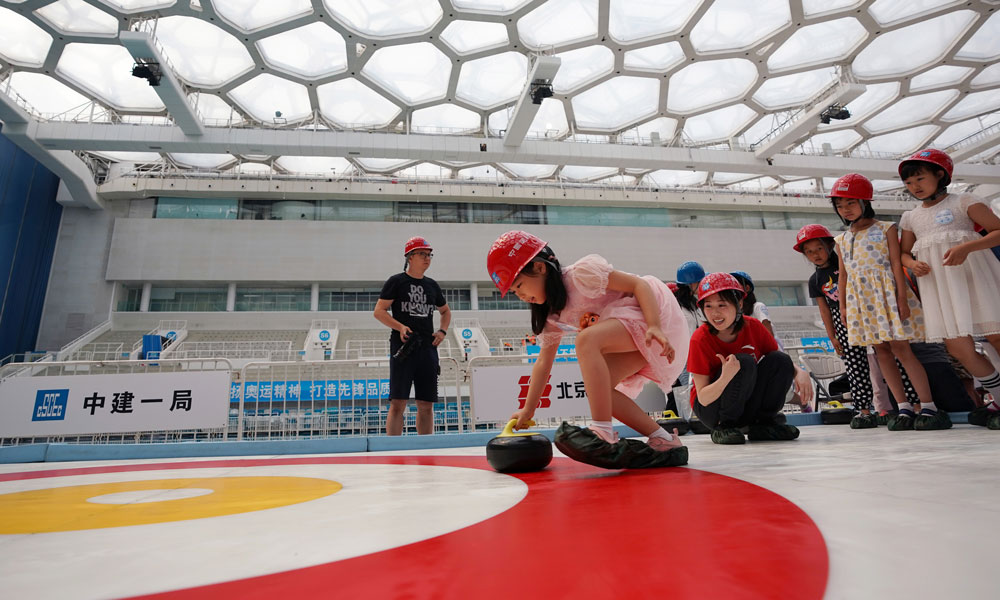 图为6月2日，一名小朋友在改造中的国家游泳中心内的简易冰壶场地体验冰壶游戏。（新华社记者 鞠焕宗 摄）