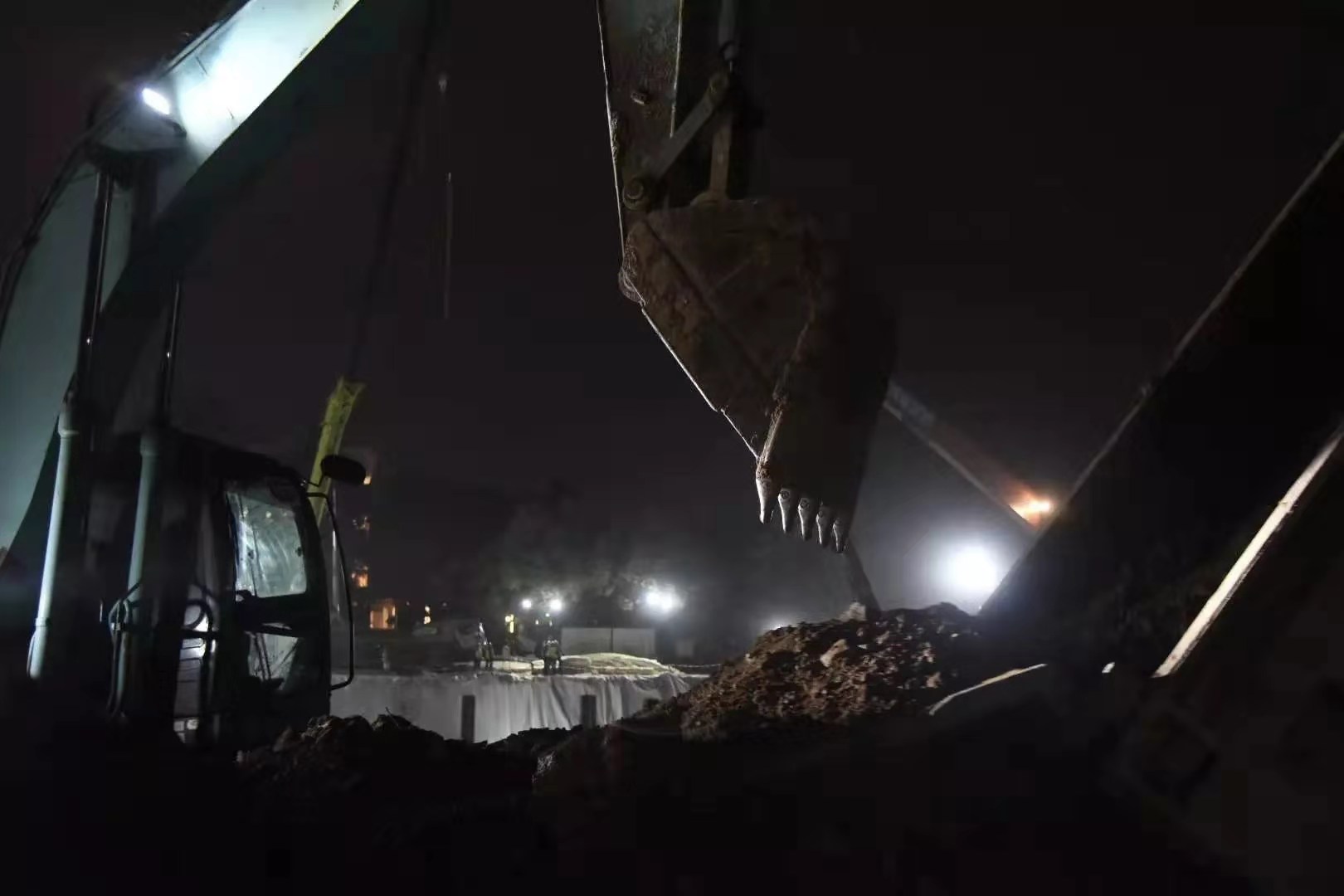 截至2月1日，火神山医院项目场地基础施工全部完成。图为2月1日20时，火神山医院蓄水池，挖掘机协助卡车卸下刚运到泥土。