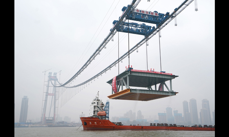 11月15日，武汉杨泗港长江大桥完成首节钢梁架设，标志着这座世界最大跨度双层悬索桥，进入桥面主体结构建设阶段。图为缆载吊机在吊装重达1000吨的钢梁。（新华社记者 程敏 摄）